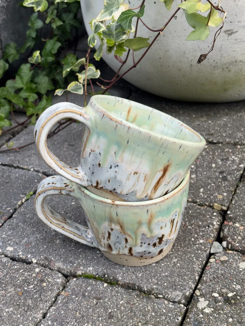 Två koppar med grön rinnande glasyr.